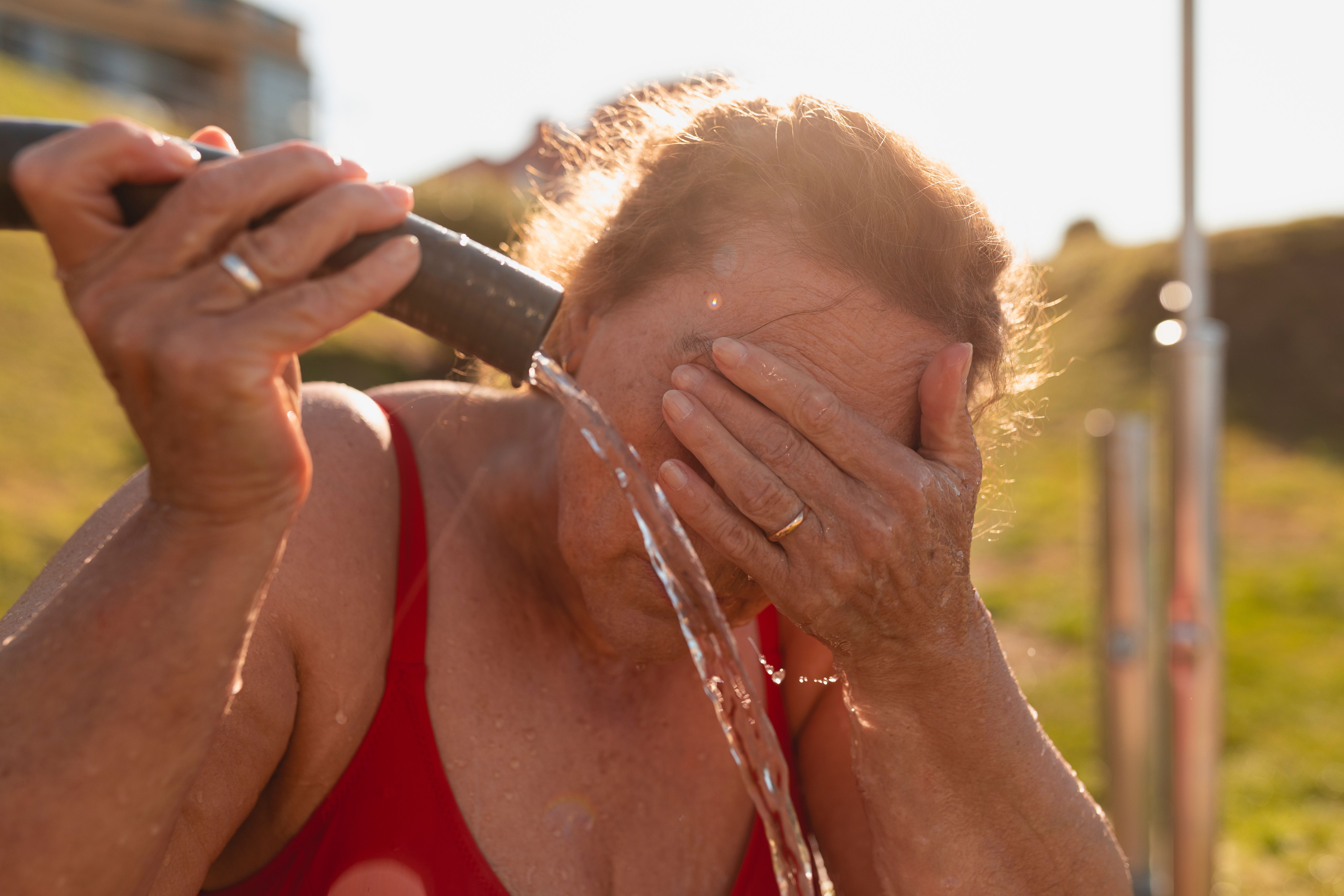 retired adult woman takes shower beach wash off saltpeter sand from her skin galicia spain (1)