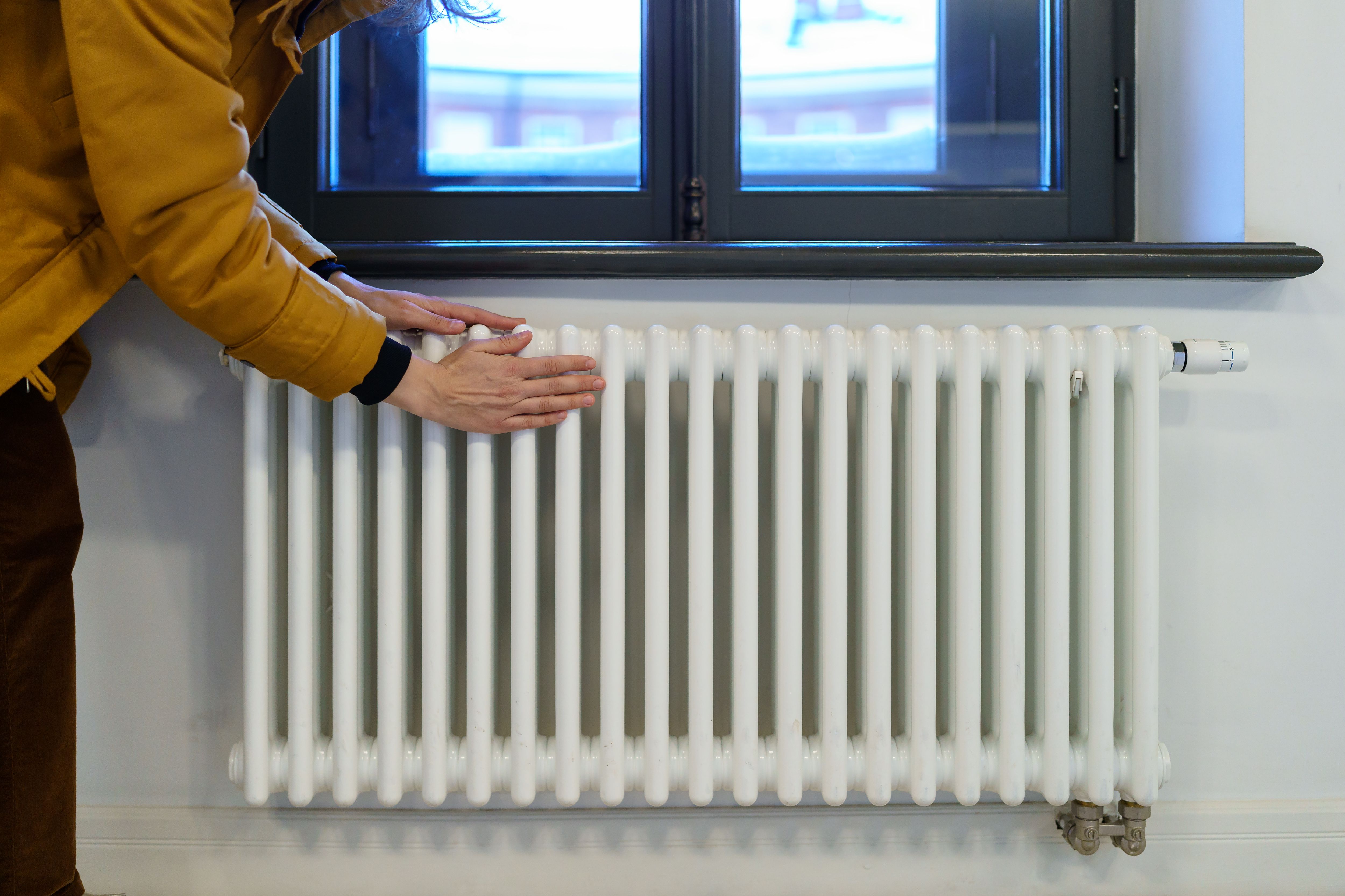 woman warming hands near heating radiator after winter walk female checking battery temperature